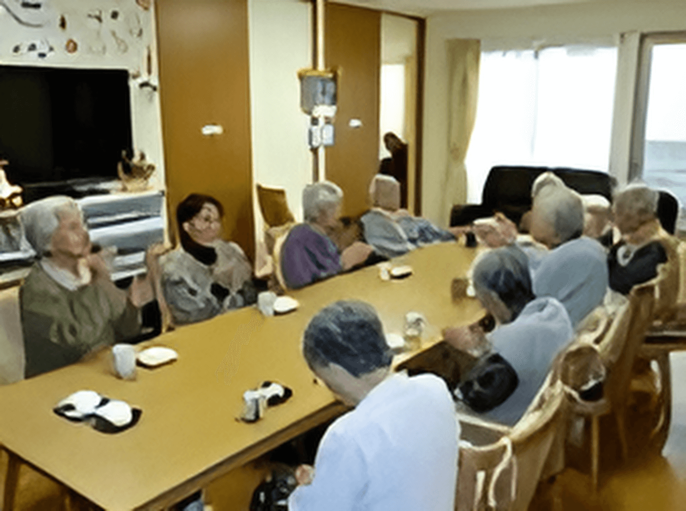 テレビや長机が置いてある施設内のリビングスペースの様子。利用者が集まっている時間
