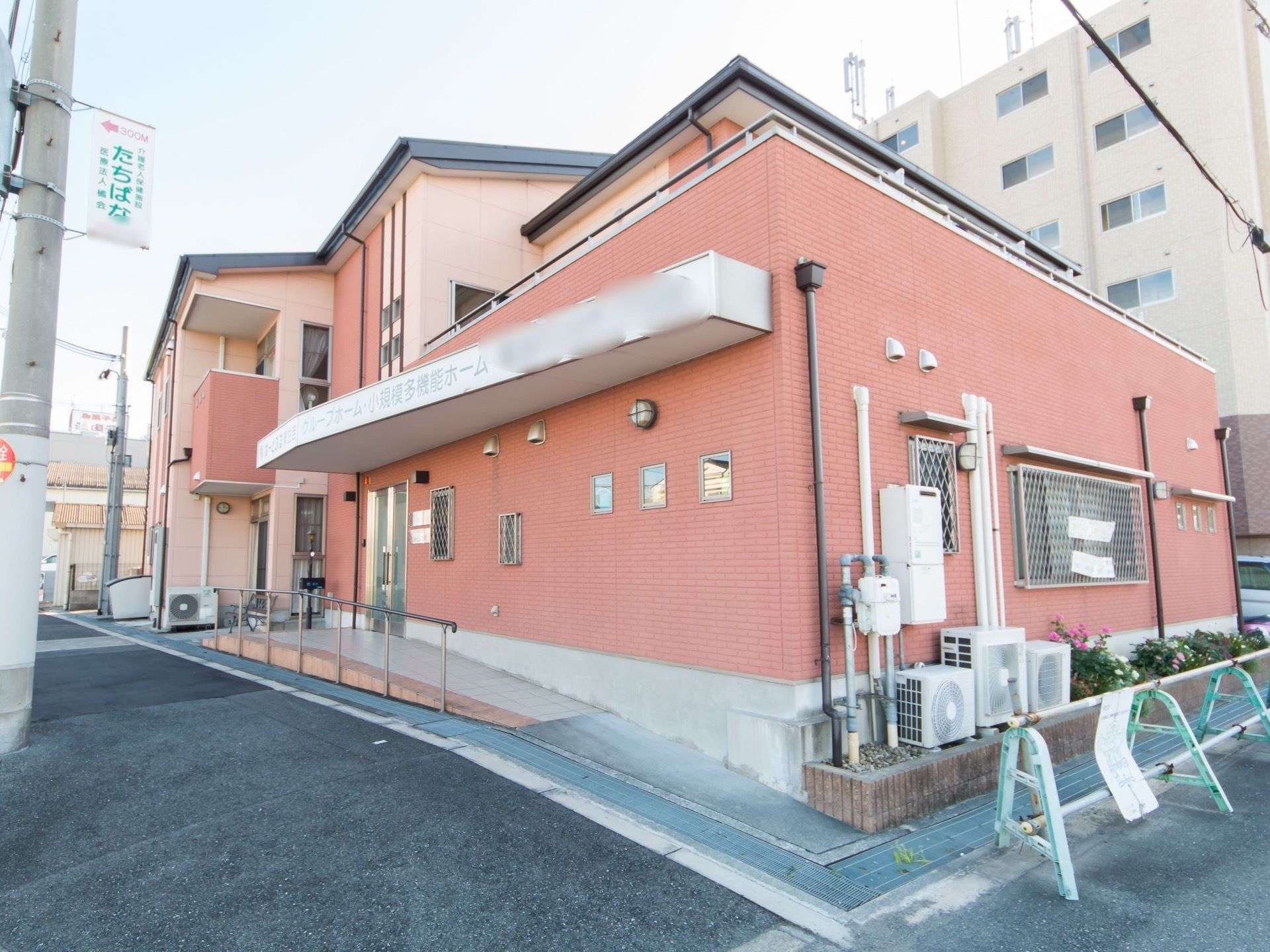 舗装された敷地に建つ施設。施設名称が明記された屋根が細長く伸びており、その下にスロープがある。