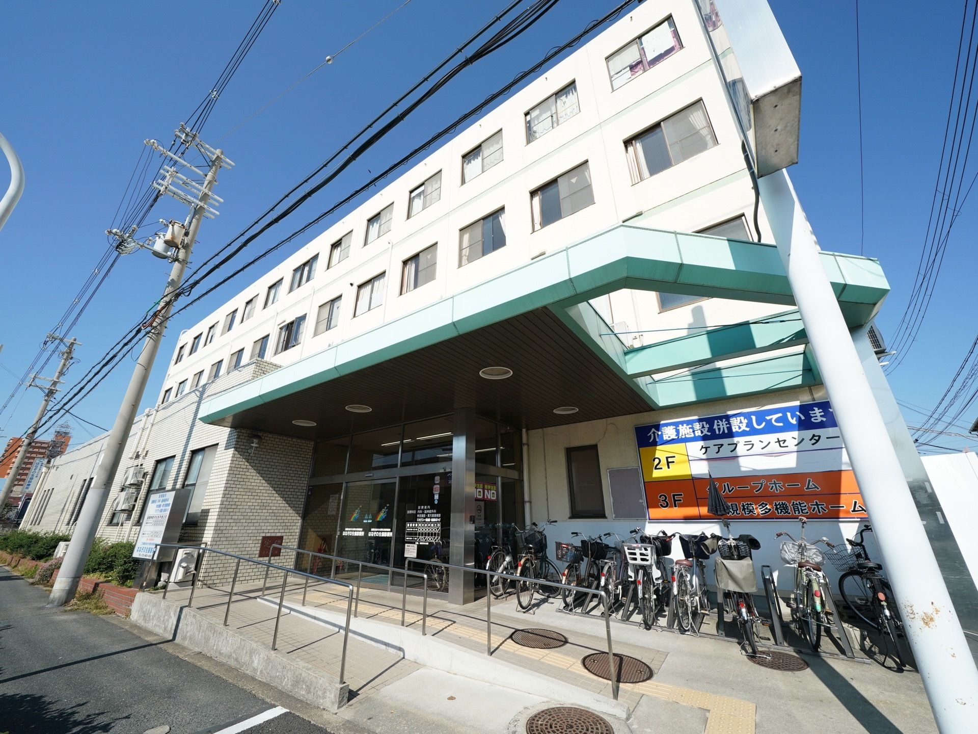 白色の壁で、三階建ての大きな建物になっている。入口の隣には駐輪場のスペースが確保されており、スロープもついている。