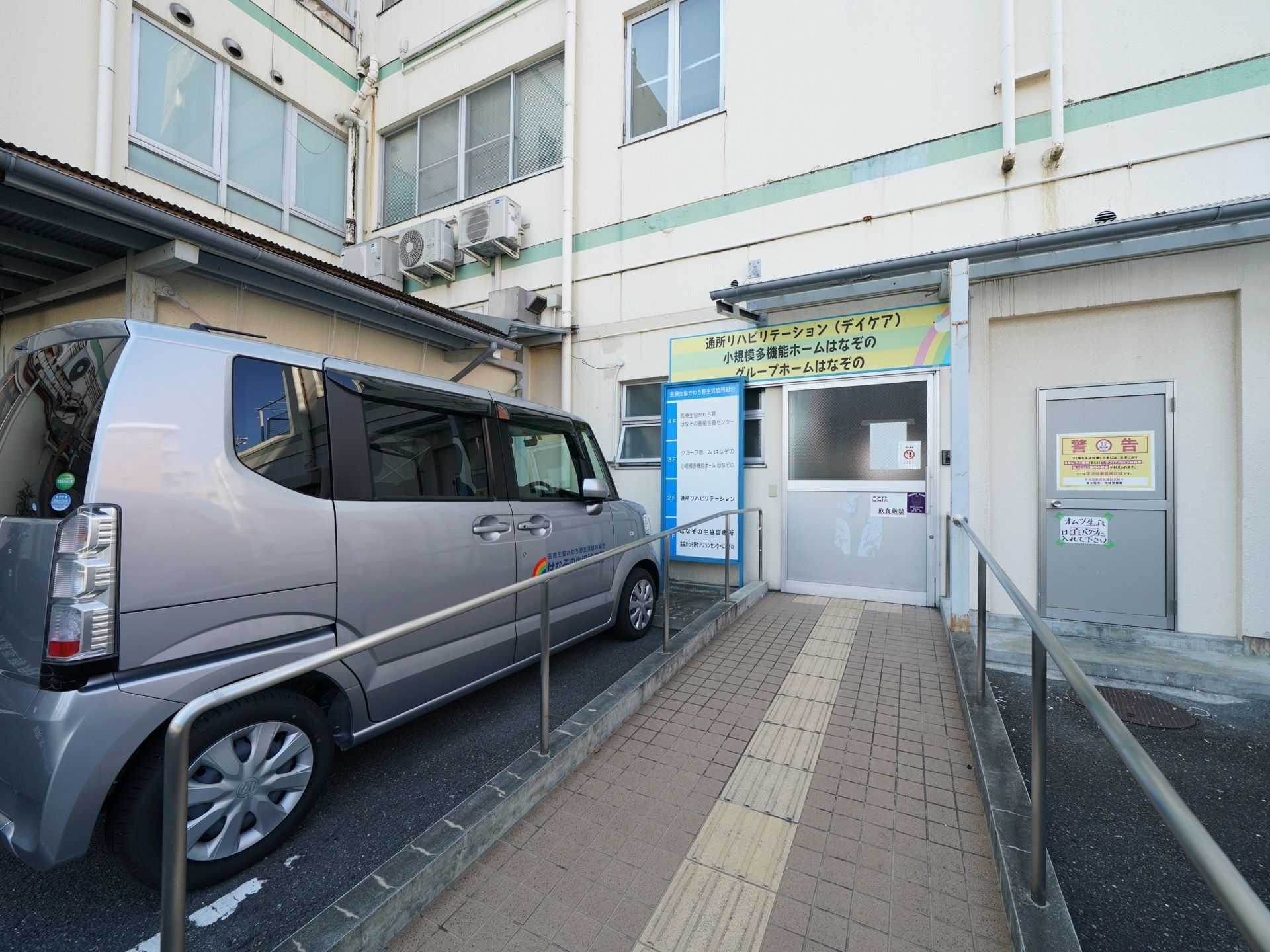 入口のすぐ側に大きな車が駐車している。スロープと手すりが完備されているので車まで移動する際にも安心感がある。