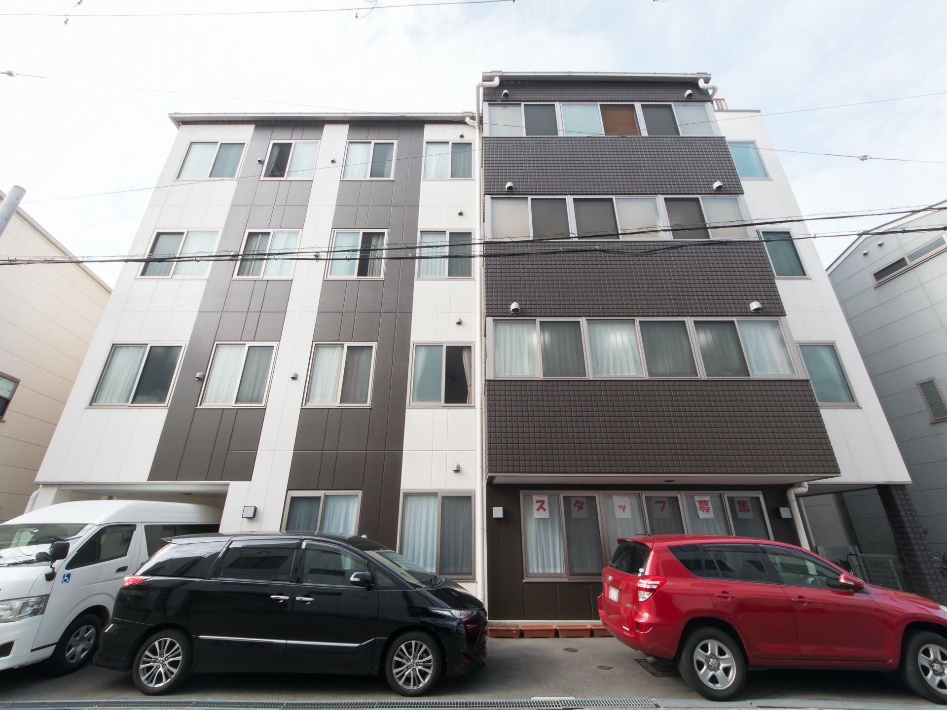 ブラウンを基調とした、スタイリッシュなデザインの４階建ての住宅。建物の前には、車が複数台停められている。