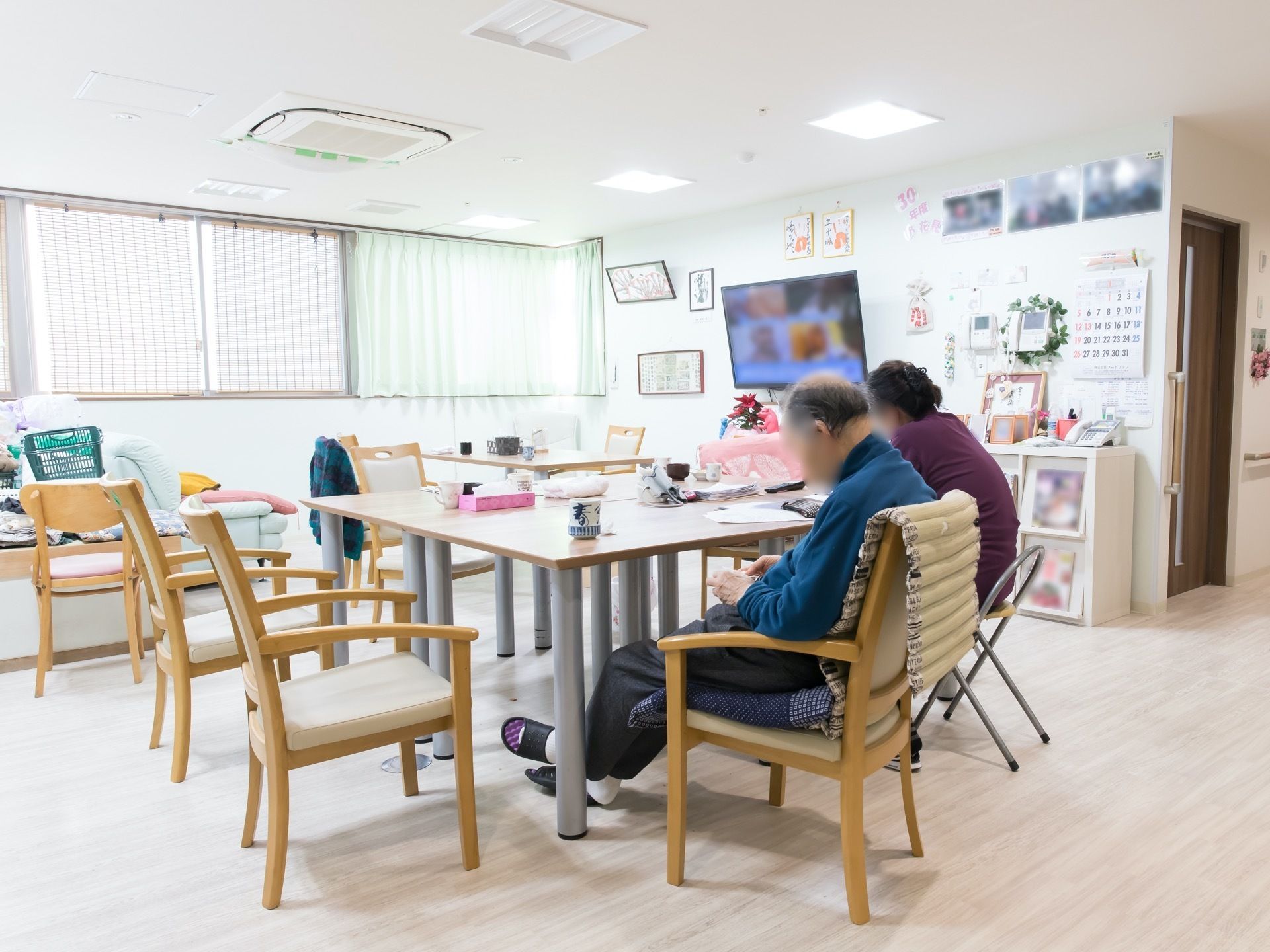大きな窓のある明るいダイニングで、壁には液晶テレビが１台取り付けられている。天井には、複数の照明が設置されている。