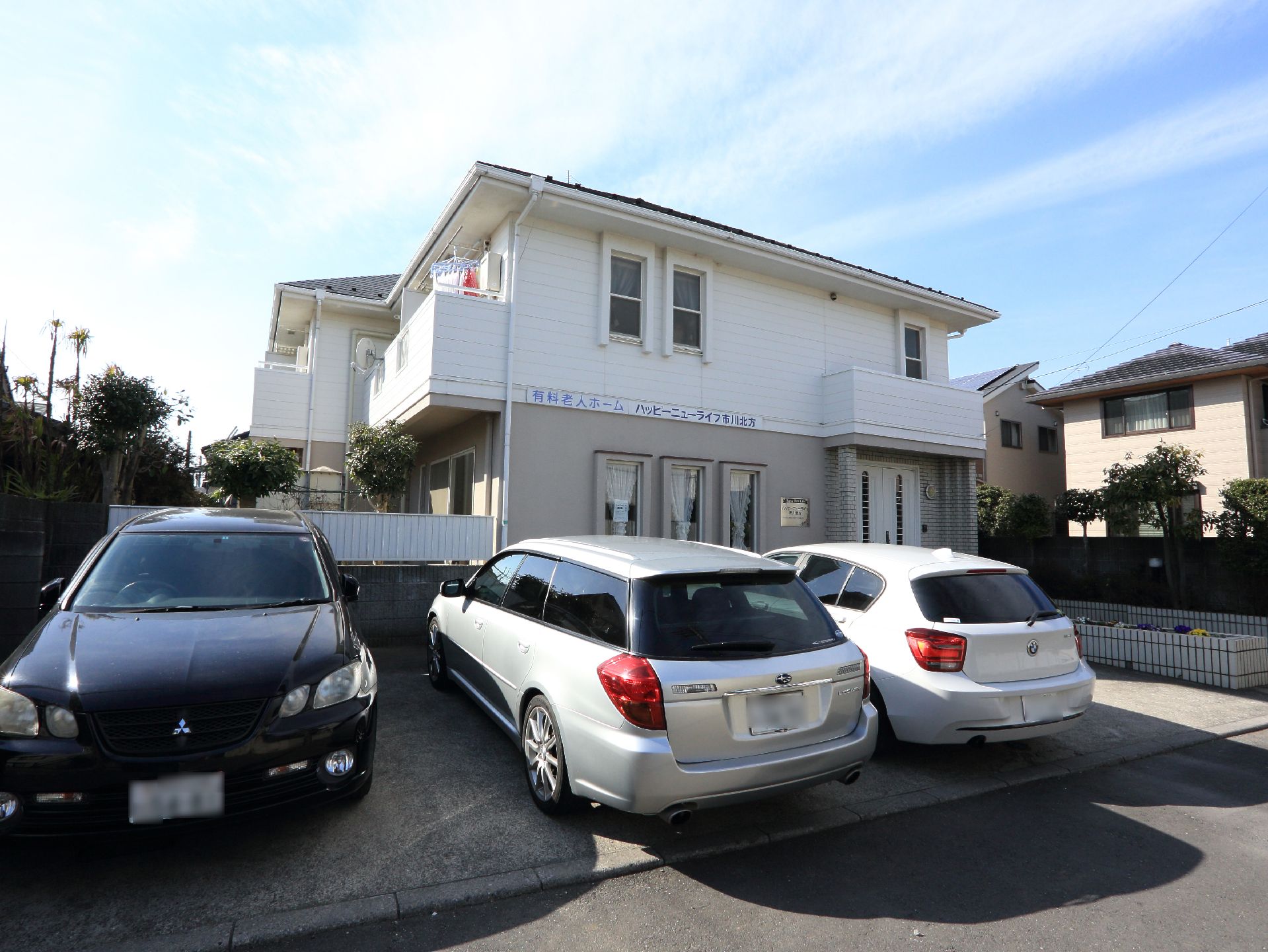 施設入口前には数台の車をとめることができるスペースがある。施設は2階建てで、外壁に施設名が表示されている。