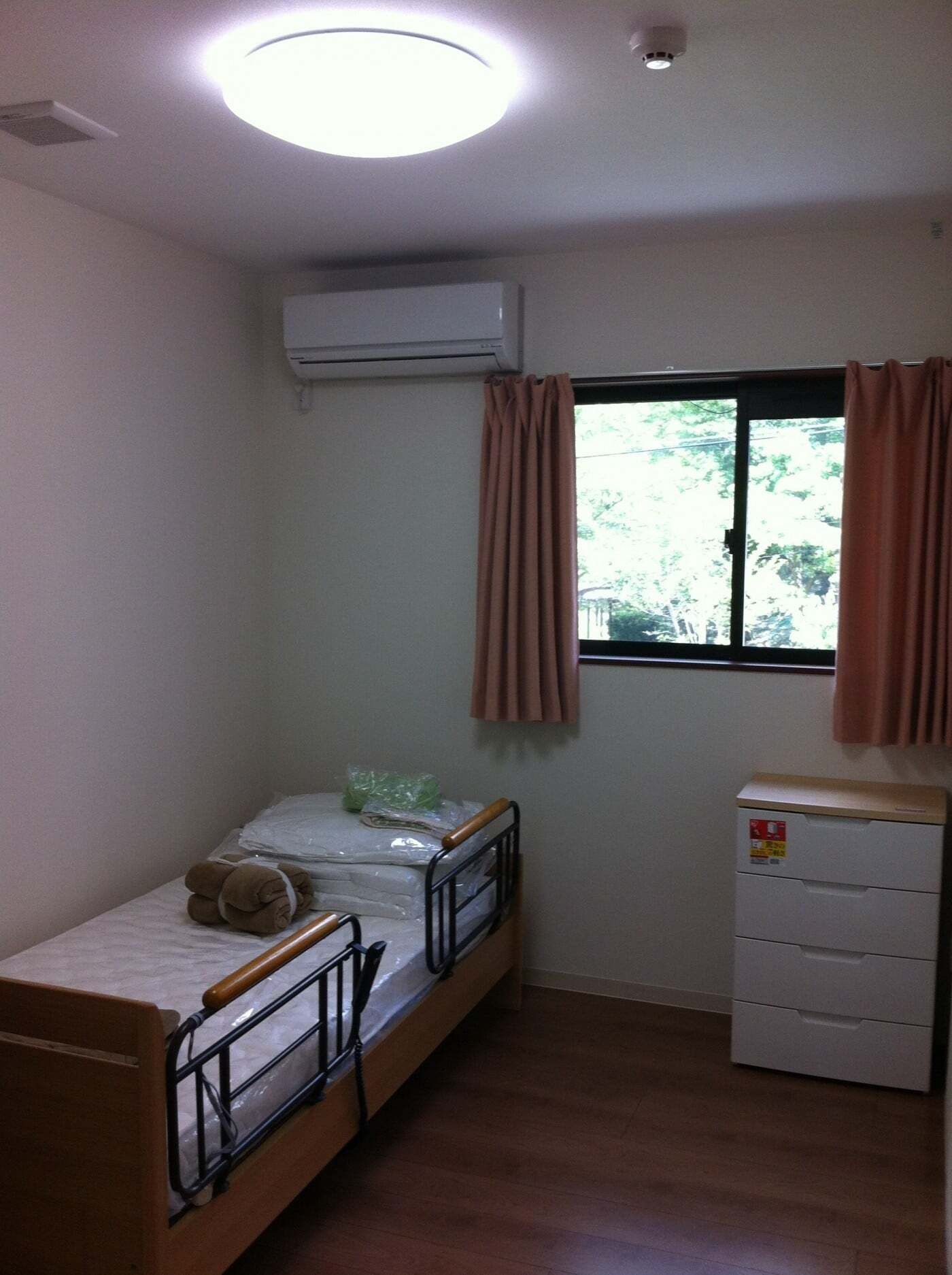 照明が付いた部屋にはカーテンが付いた大きな窓があり、寝具付きのベッドやタンスが置かれている。
