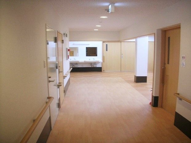 幅の広い廊下は手すりが全面的に設置されている。廊下の床と同じベージュの手すりが白い壁のアクセントとなっている。