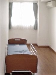 フローリングの居室には大きな窓とエアコンが付き、介護用ベッドが置かれている。