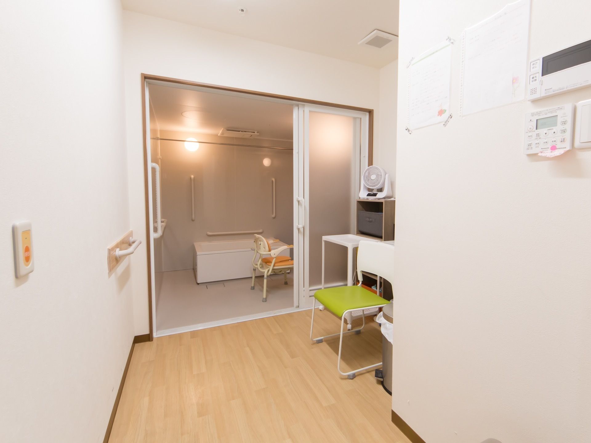 脱衣所と浴室の間に３枚スライドの扉がついている。脱衣所の白い壁には、手すりや緊急呼び出しブザーが設置されている。