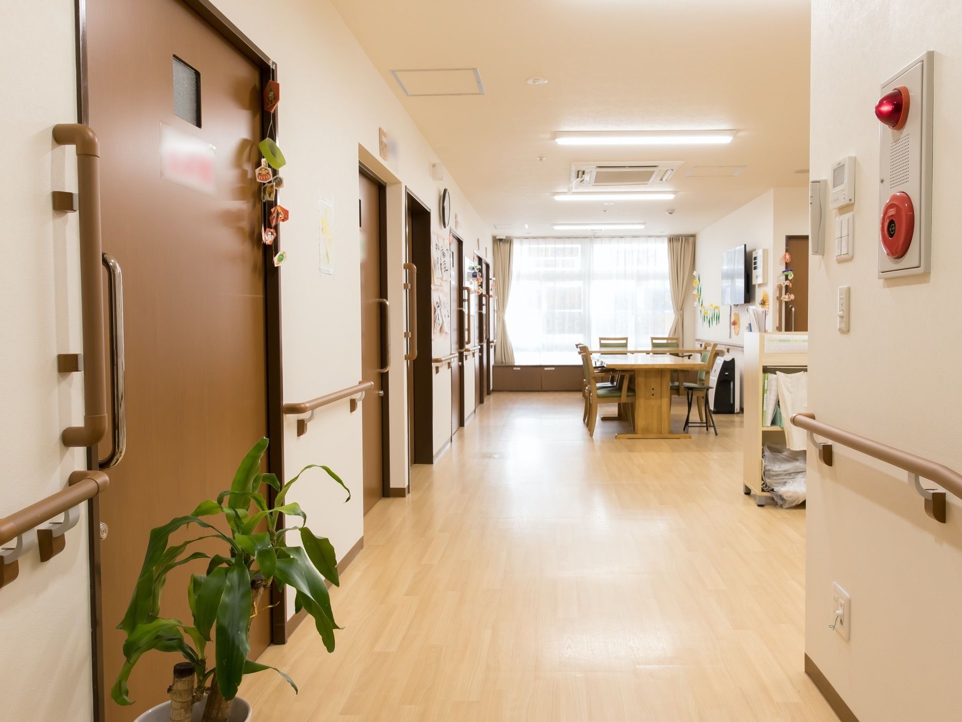 居室前の廊下からフラットな床面でフロアーへと続いている。白い壁には、非常ベルや手すりが設置されている。
