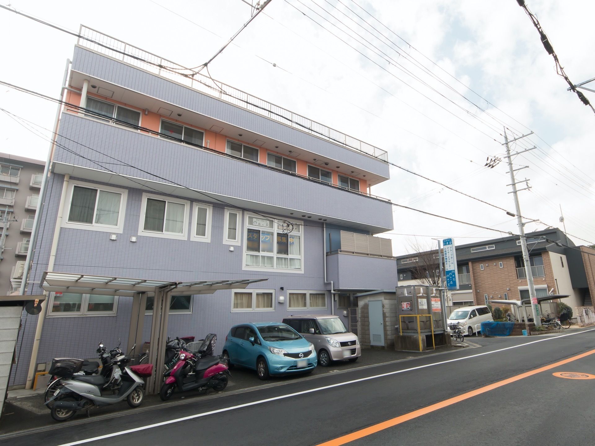 屋上を完備した3階建ての施設外観である。駐車スペースの隣には、テラス屋根が設置された駐輪スペースが設けられている。