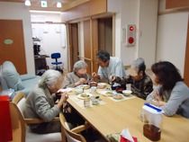 食堂のテーブルを囲み食事を楽しむ入居者と見守るスタッフ。