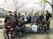 桜の花が満開にさいたきれいな風景をバックに入居者とスタッフが記念撮影。