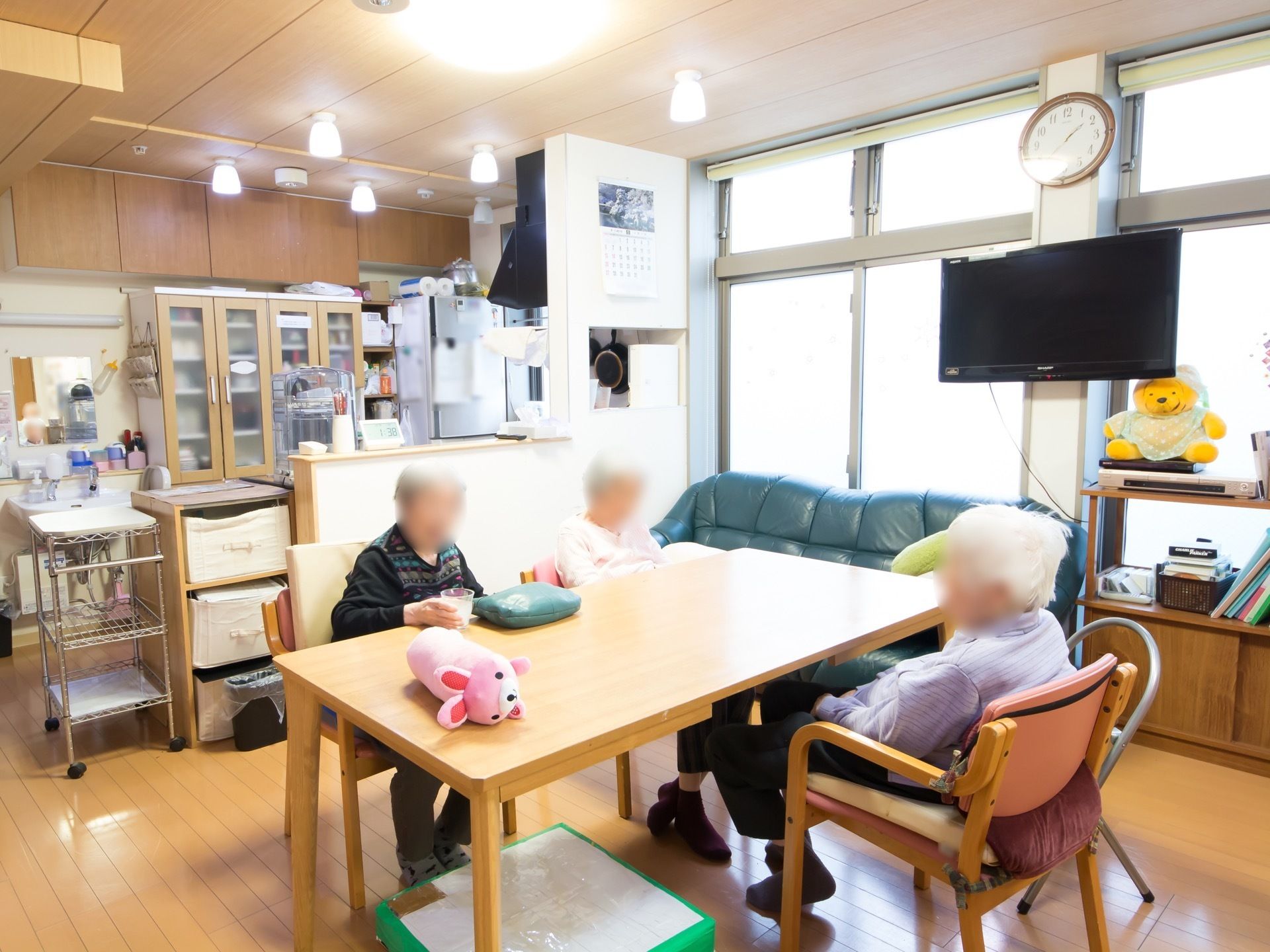 食堂の窓際の柱に、時計と壁掛けテレビが設置されている。かわいい動物のぬいぐるみがテーブルの上に置かれている。