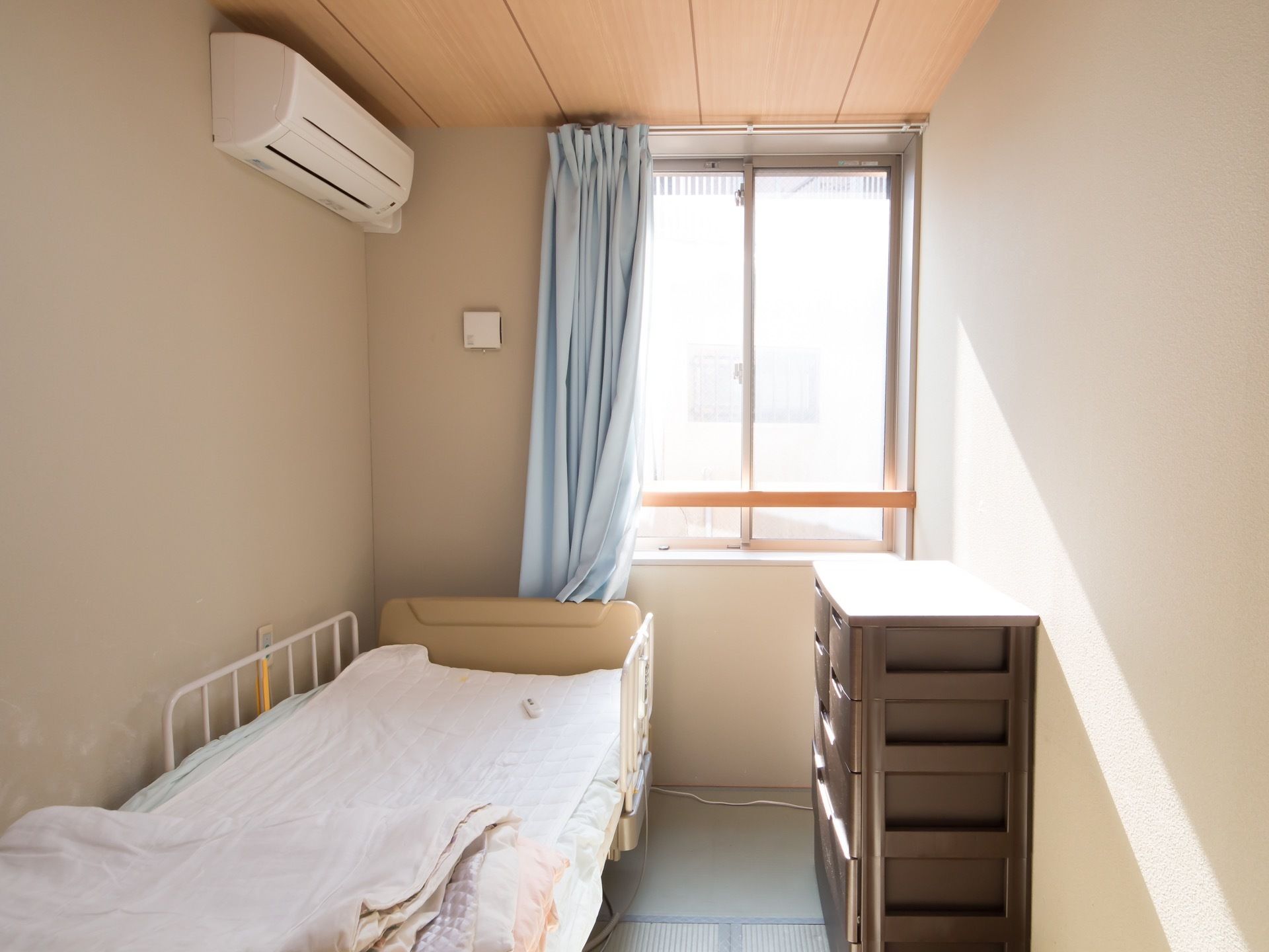 居室に窓からの日差しが入り込んでいる。転落防止柵つきのベッドが設置されている。床面は畳敷きになっている。