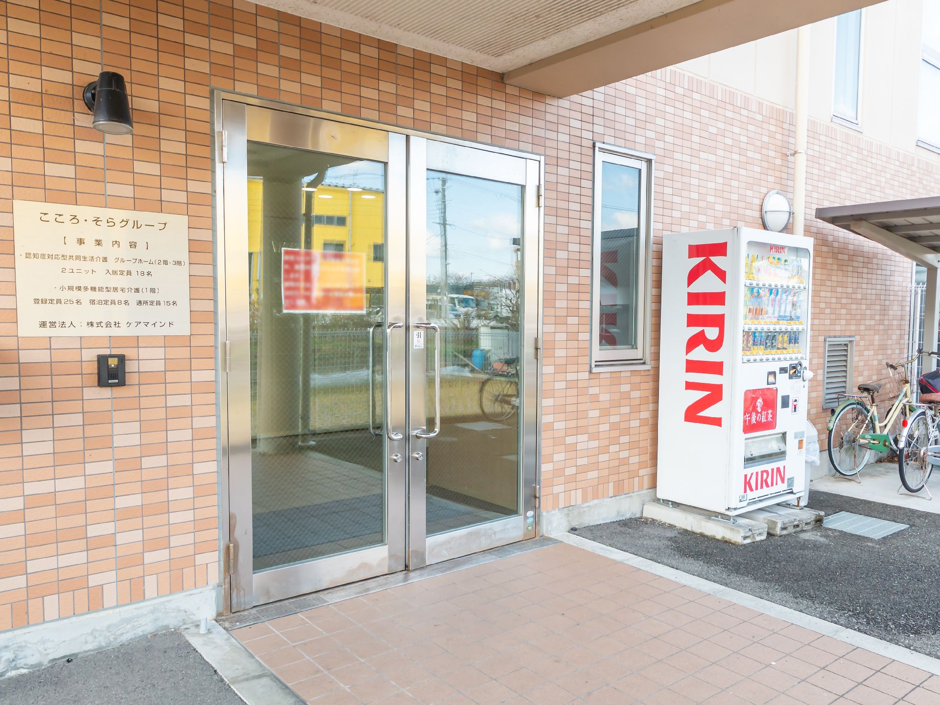 水の入ったコップを持ったエプロンを付けた若い女性スタッフが薬を飲もうとしている高齢女性のそばで待っている。