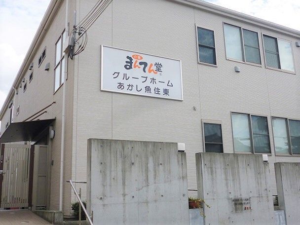 ベージュ系の2階建ての建物。玄関には屋根が付き、窓もたくさんついている。