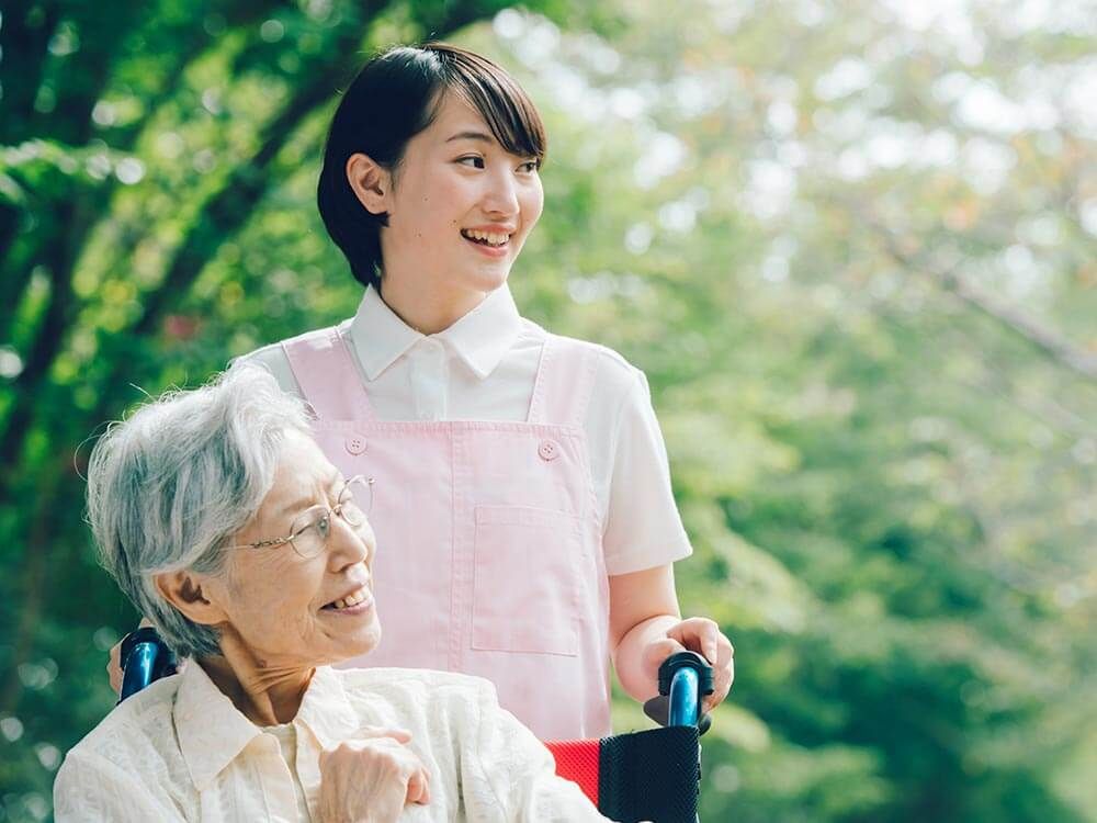 自然の中を散歩する車椅子に乗った高齢女性と介助をする女性ヘルパー