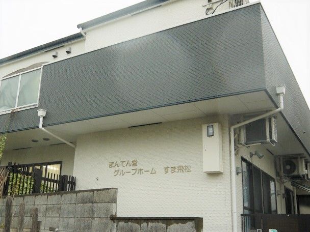 白とダークグレーの2階建ての建物。外壁にはホーム名が描かれていて、一般の民家のようなデザイン。