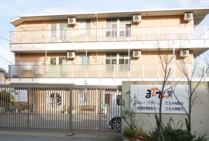 3階建ての建物。ベージュでまとめられ、温かい雰囲気の外観。駐車場があり、ホーム周辺には緑もたくさん植えられている。