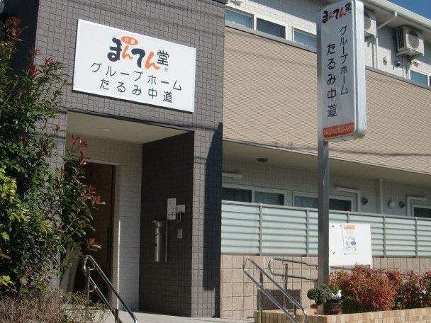 2階建ての建物。2階部分にはベランダがあり、ホームの玄関の屋根にホーム名が書かれたプレートが貼られ、看板も立っている。