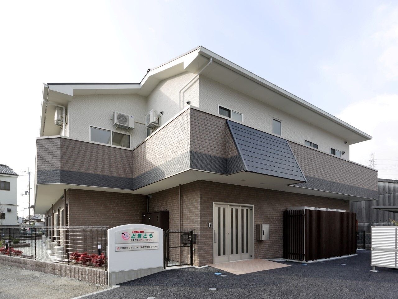 ベランダ付きの2階建ての建物。三角屋根が付き、玄関にはスロープもある。