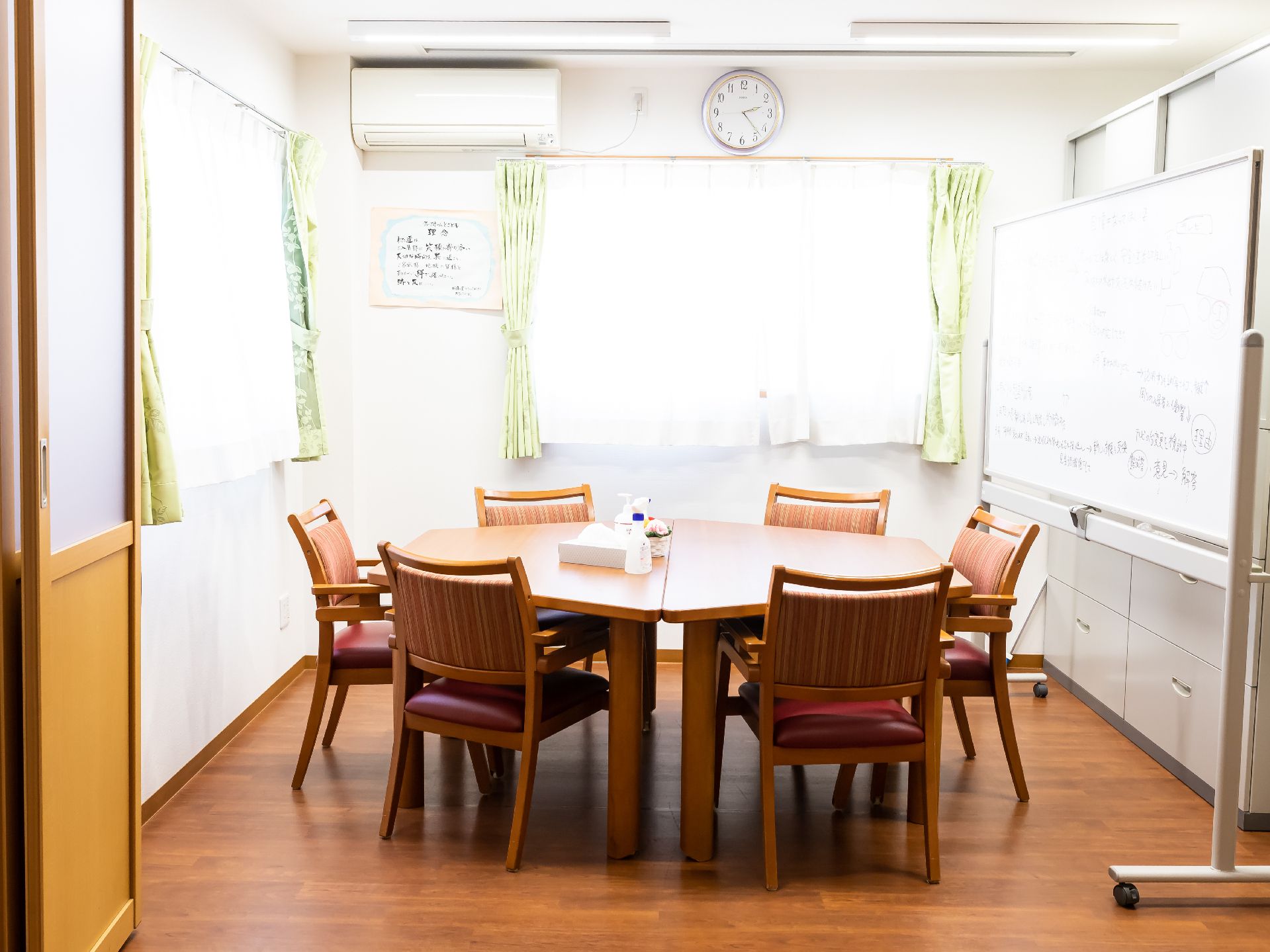 ホワイドボードが置かれ、丸いテーブルに椅子が置かれている共有スペース