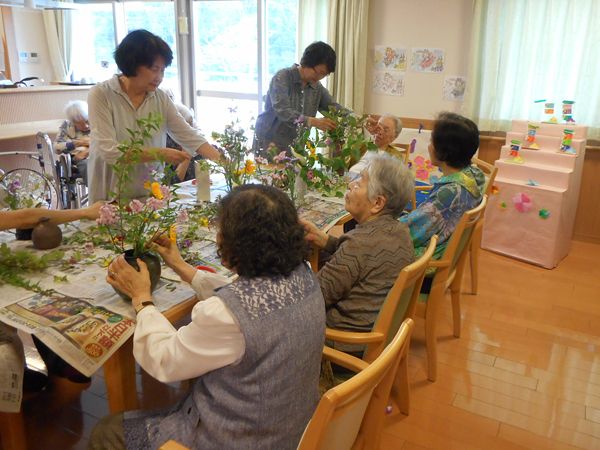 フラワーアレンジメントを楽しむ入居の様子。木製のテーブルの上には新聞紙と花が広げられている。
