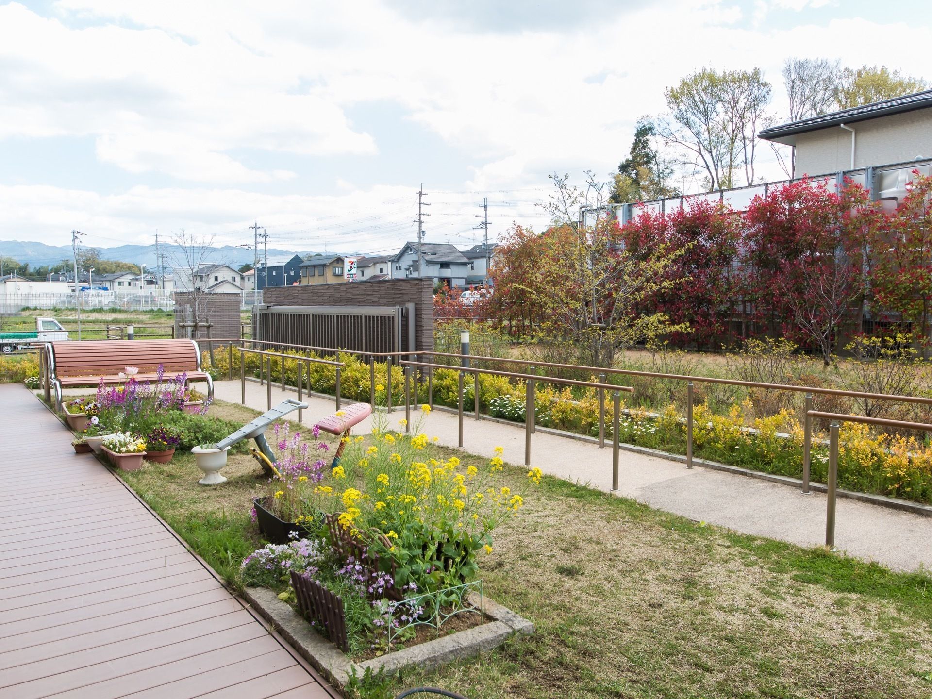 施設敷地内に庭園が設けられている。両側に手すりが設置された散策路がある。芝生の上に木製ベンチが置かれている。