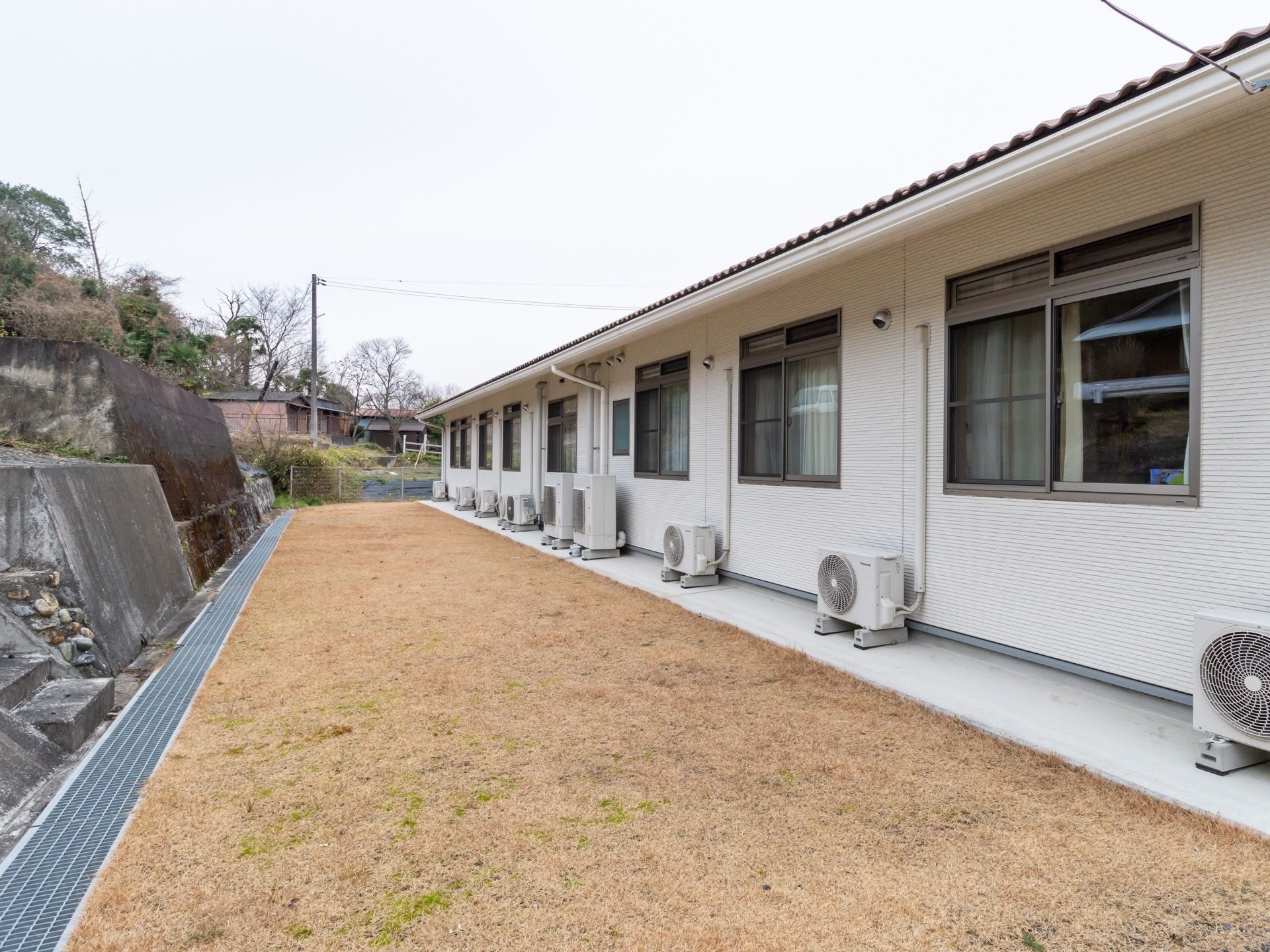 １階建てで奥行きのある建物。裏手は芝生になっている。軒下に室外機が置かれているほかは、物が置かれておらず、掃除も行き届いている。