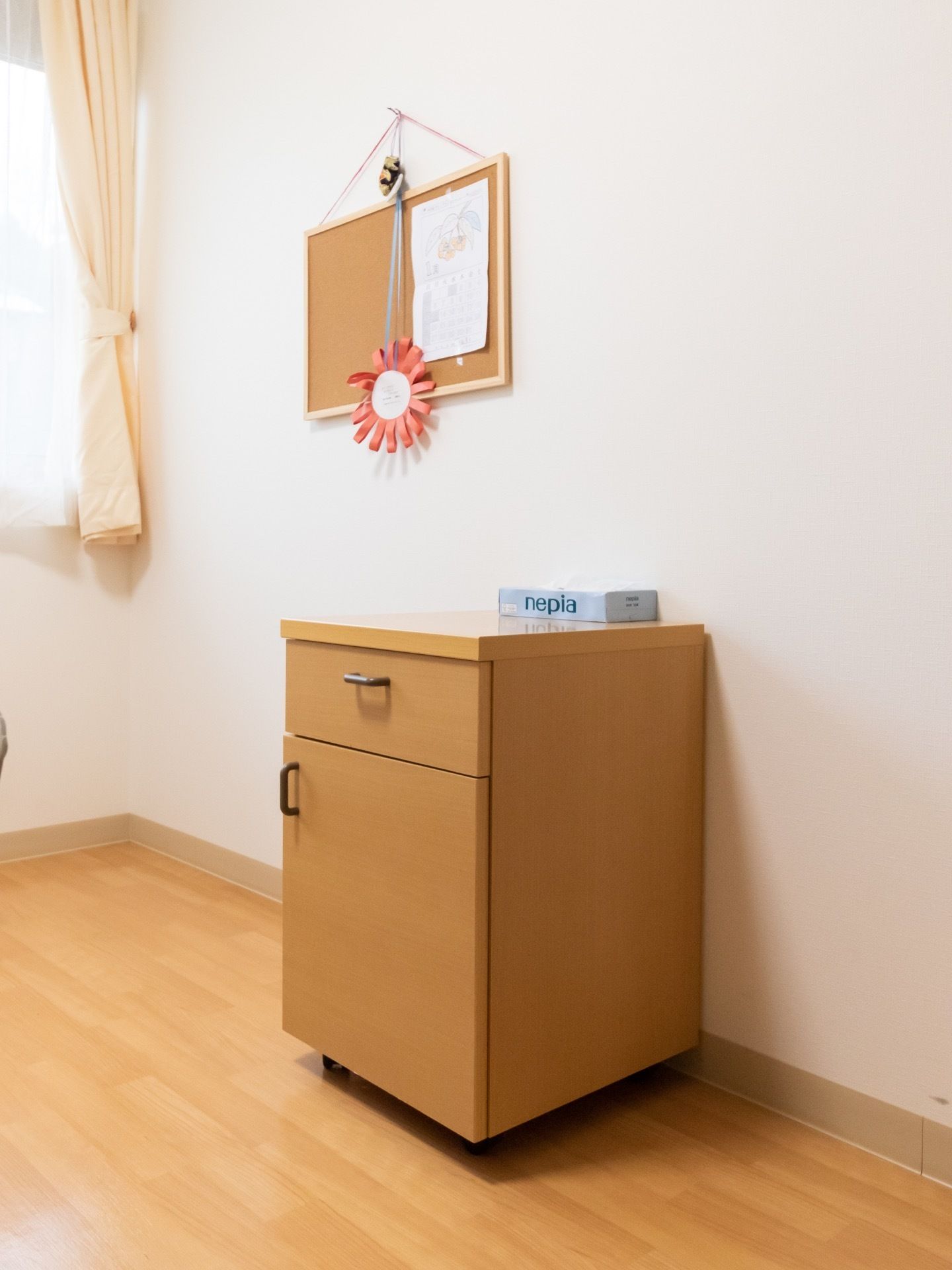 部屋には小物を収納することができる棚が設置されている。その上にはティッシュが置かれている。壁にはコルクボードが掛けられている。