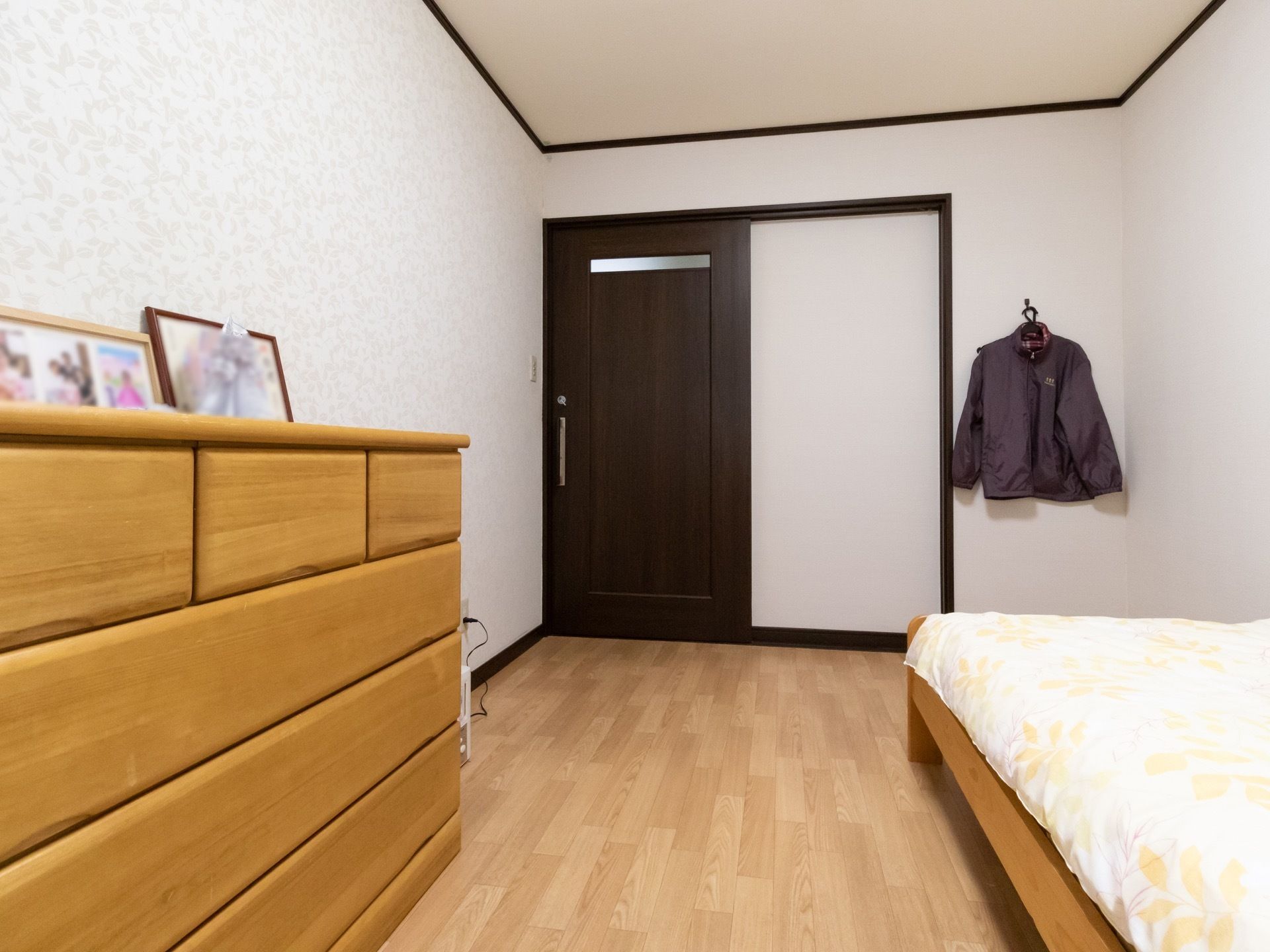 居室は間口の広い横開きの扉で、床は段差のないフローリングである。壁にはジャケットが掛けられ、タンスの上には写真が飾られている。