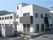 白い壁の２階建ての建物。青空が広がる向こう側に山が連なっている様子