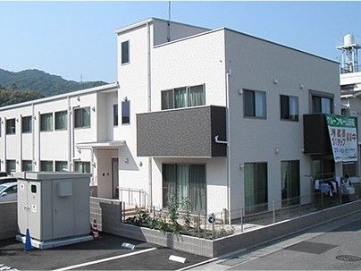 白い壁の２階建ての建物。青空が広がる向こう側に山が連なっている様子