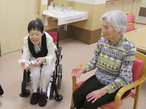 椅子に座った女性入居者と車いすの女性入居者が一緒にレクリエーションを楽しむ様子。