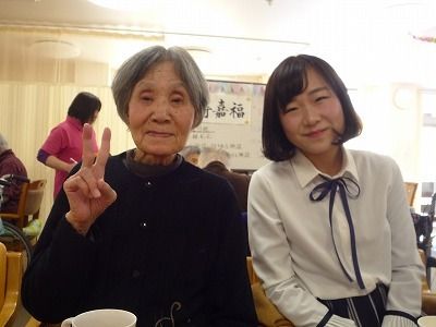 制服を着た女生徒と女性入居者が並んで座り、楽しそうにカメラに向かって微笑んでいる様子。