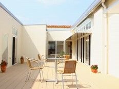 広々としたウッドデッキのテラスの中央には円形のテーブルといすのセットが置かれ、鉢植えが複数飾られている。