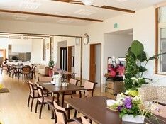 花や草木がたくさん飾られた共有スペース。ブラウン系のテーブルが並び、壁には時計も飾られ、日当たりも良好。