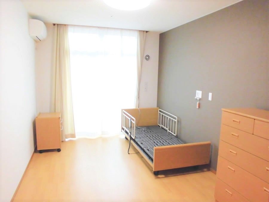 大きな窓があり明るい雰囲気。居室には、ベッドや収納家具だけでなく照明やエアコンもついている。