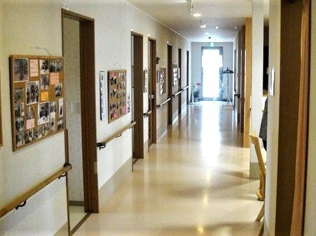 まっすぐな廊下と壁に貼られた写真類が印象的な写真。手すりがついた廊下の様子