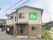 大きめの一軒家風のデザインの建物。奥のほうに住宅街と自然豊かな場所がある