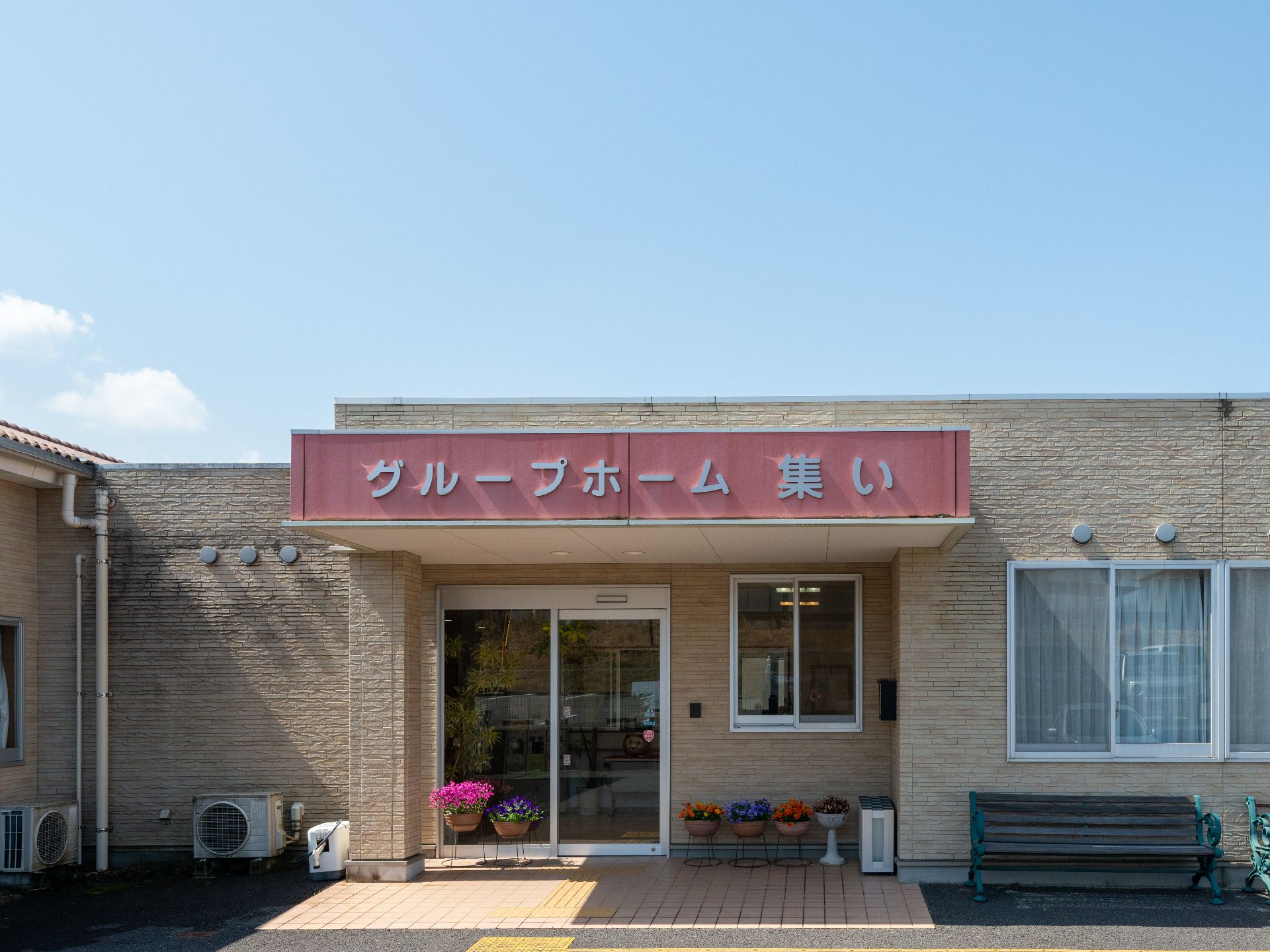 赤い玄関の屋根にはホーム名が書かれていて、日当たりのいい場所に建っている平屋建ての建物。玄関まで点字ブロックも敷かれている。