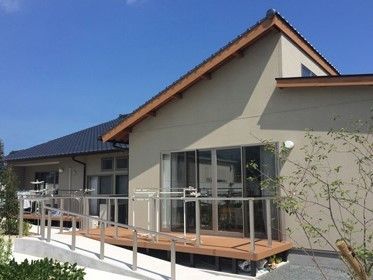 三角屋根の平屋建ての建物。外壁はベージュでまとめられており、玄関周りにはスロープがある。