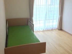 ベッドが置かれたフローリングの居室。窓が大きく明るい雰囲気。