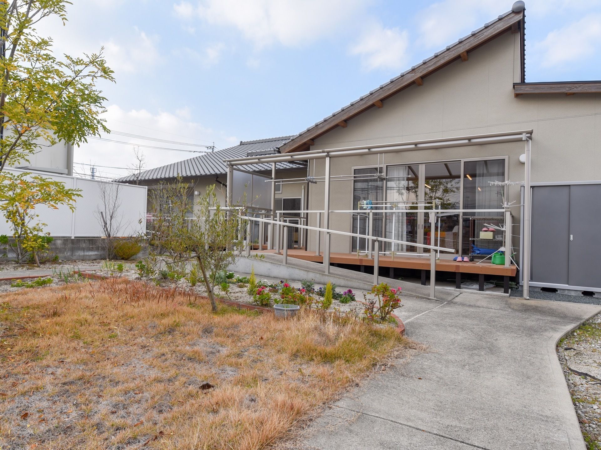 平屋建てで瓦屋根の和風の建物がある。ガラス張りの玄関ドアまではスロープになっており、手すりが設置されている。
