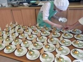 白衣にマスク、帽子、グリーンのエプロンを付けたスタッフが料理の盛り付けをしている様子。