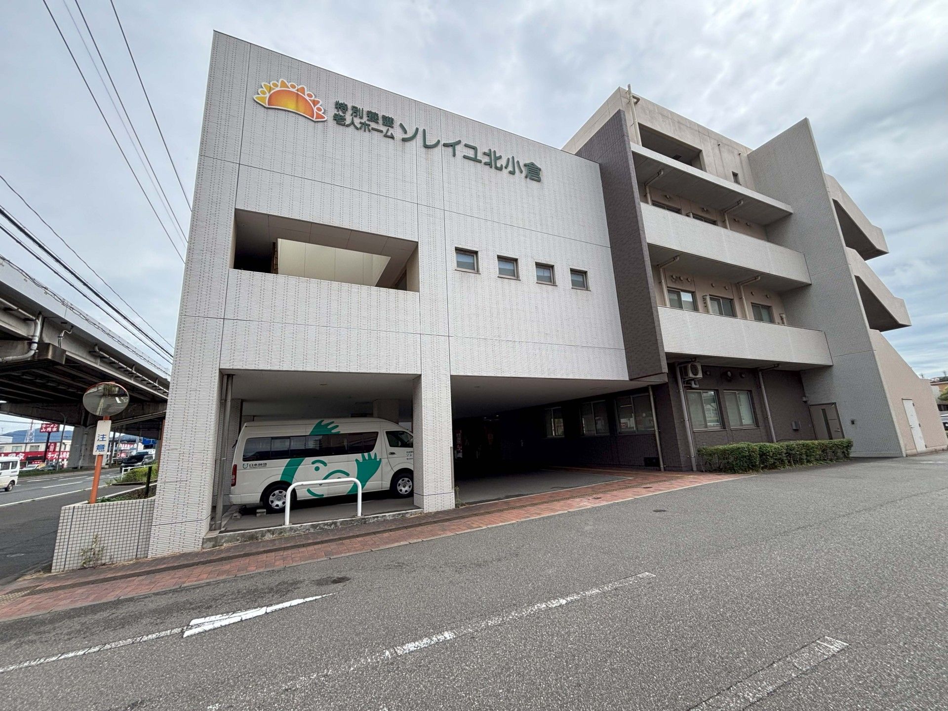 屋外で楽しそうに過ごしている高齢所男女と若い男女のスタッフ。中央にいる高齢女性は車いすに座り、ハンドルを高齢男性が握っている。