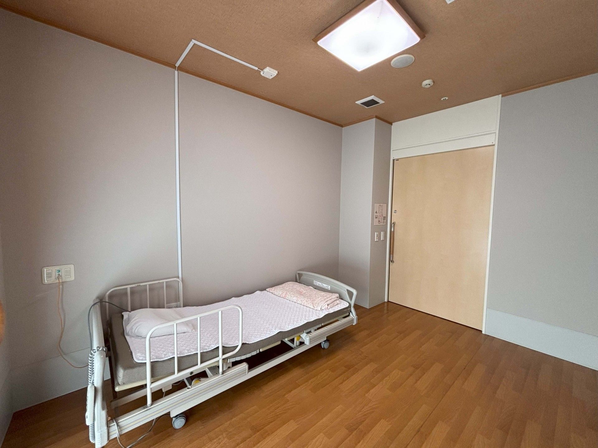 日当たりのいい屋内で車いすの高齢女性に若い女性スタッフが付き添っている。女性は指さす方向を見てスタッフが一緒に笑っている。