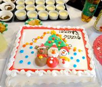 サンタクロースやトナカイ、スノーマンなどがクリスマスツリーの前に並んで立っている白をベースとしたクリスマスケーキ。