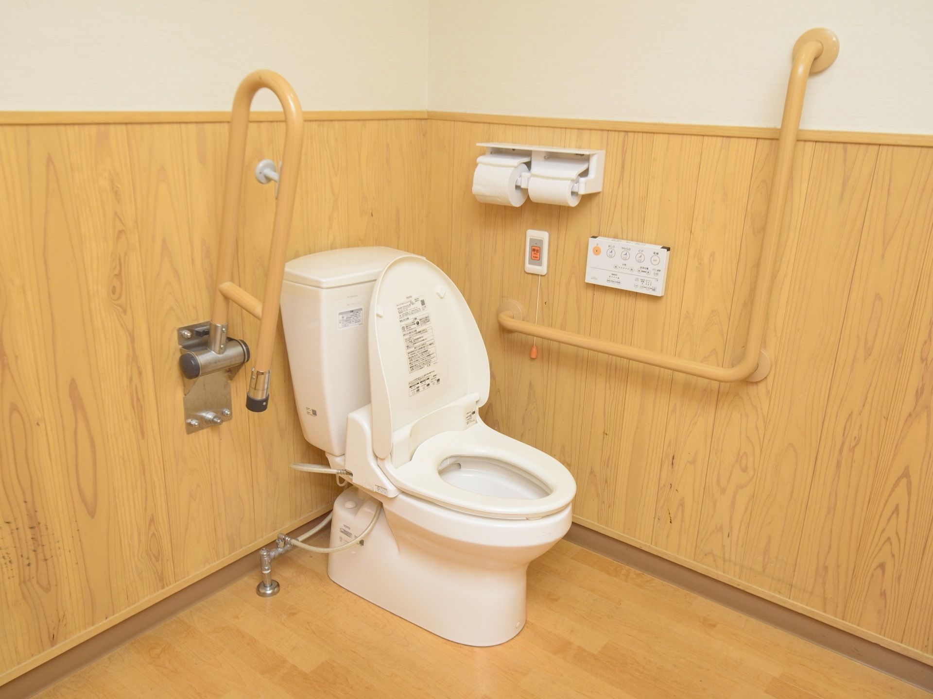 トイレの壁には、可動式とＬ型手すり、呼び出しボタンが取り付けられており、温水洗浄便座が便器に設置されている。
