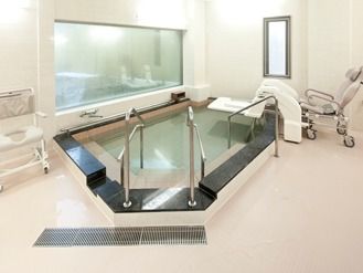 大浴場の様子。手すりが取り付けてある大きめの浴槽、奥のほうに介護仕様のチェアがある