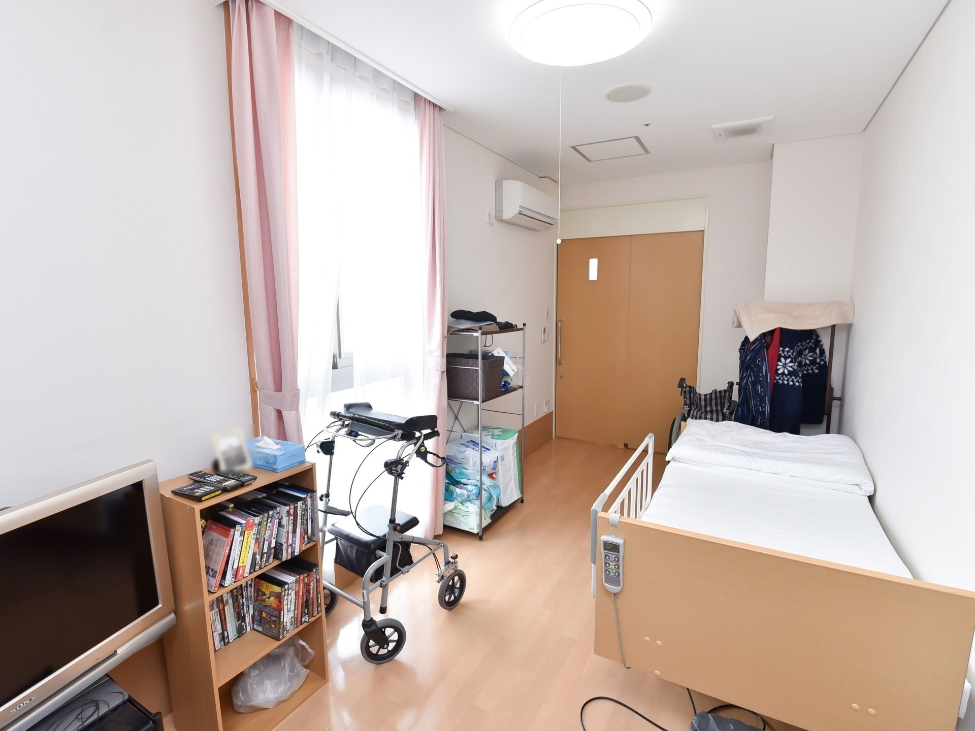 大きな窓がある明るい居室である。ベッドがあり、転落を防止する柵が取りつけられている。エアコンがあるので快適に過ごすことができる。